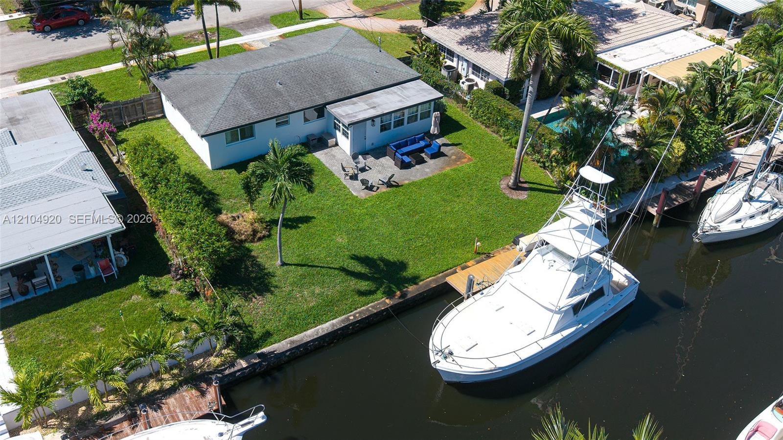 Waterfront property featuring a private bulkhead dock, expansive lawn, stone-paver patio, and mature palm trees