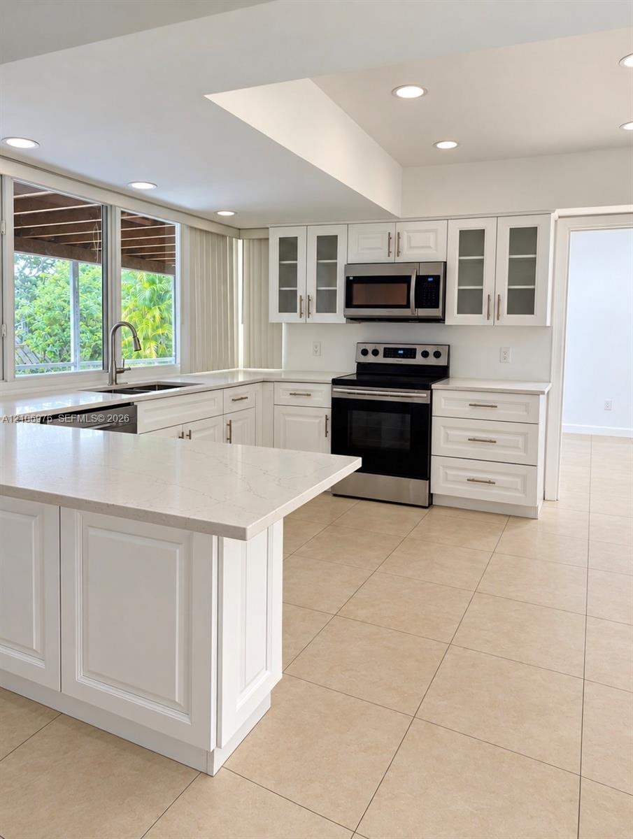 Kitchen featuring white Shaker-style cabinetry, quartz countertops, stainless steel appliances, tile flooring, and glass-paneled upper cabinets