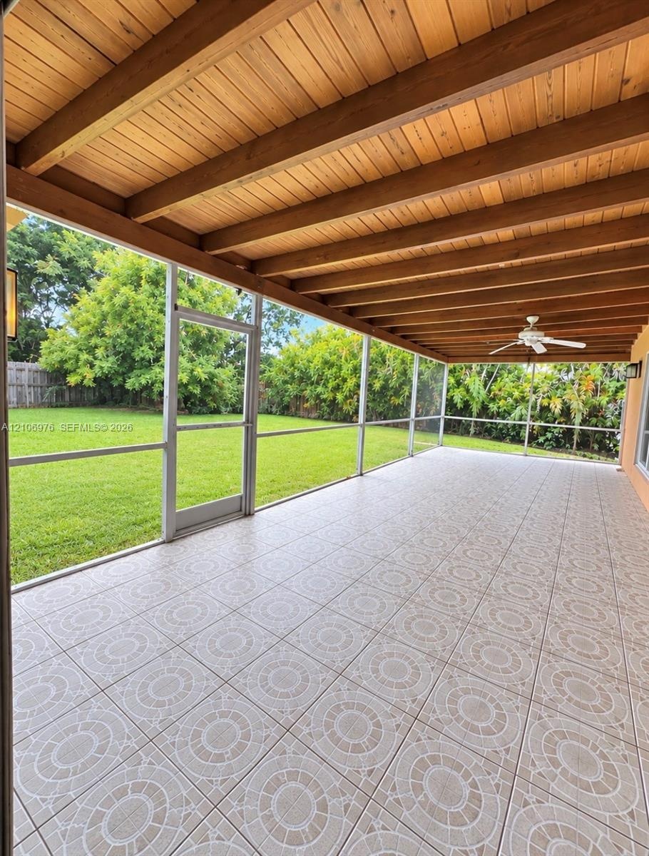 Screened-in patio featuring decorative tile flooring, exposed wood-beam ceiling, ceiling fan, and lawn access