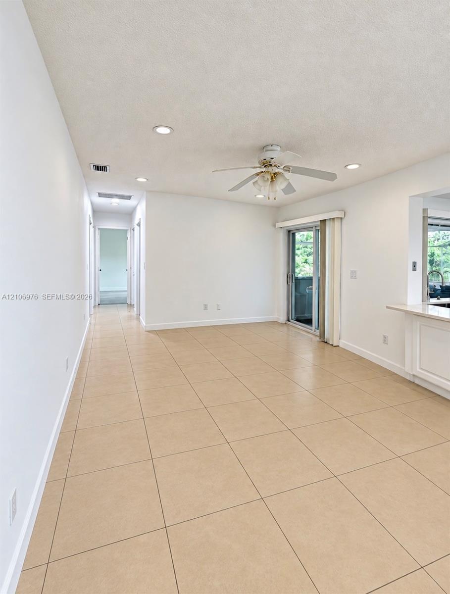 Neutral-toned tile flooring, recessed ceiling lighting, a white ceiling fan with integrated light fixture, and a sliding glass door providing external