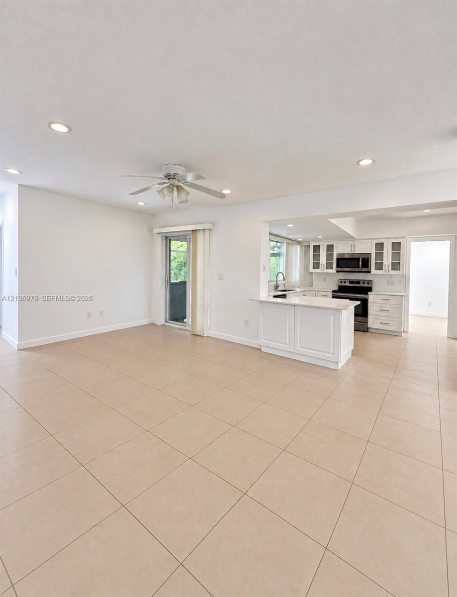 Spacious open-concept living area featuring neutral tile flooring throughout, recessed ceiling lighting, and a ceiling fan