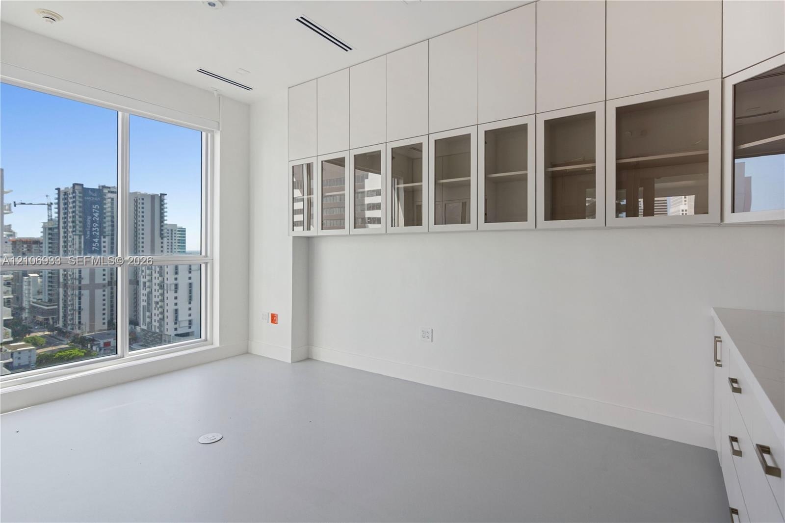 Floor-to-ceiling windows, built-in floor-to-ceiling cabinetry with glass-paneled upper doors, sleek cabinetry hardware, and solid-surface flooring