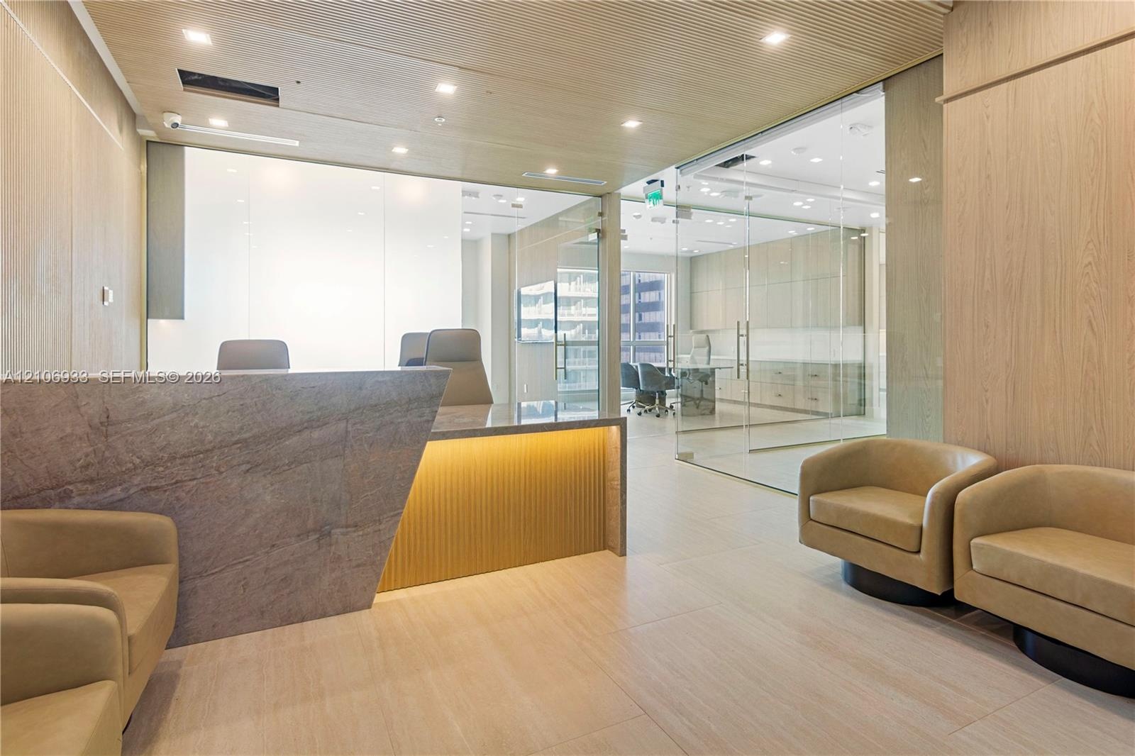 Reception area featuring a stone-faced desk with accent lighting, light wood-finished wall paneling, glass-enclosed office partitions, recessed ceilin