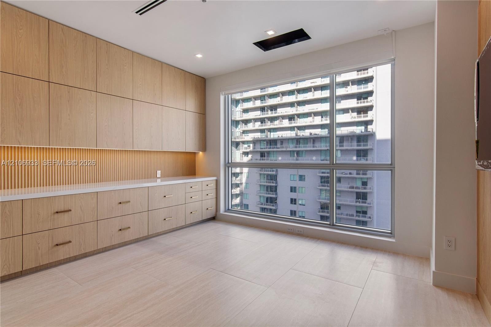 Built-in light-tone wood cabinetry with integrated storage, fluted wood detailing, smooth-surface countertops, and large picture windows