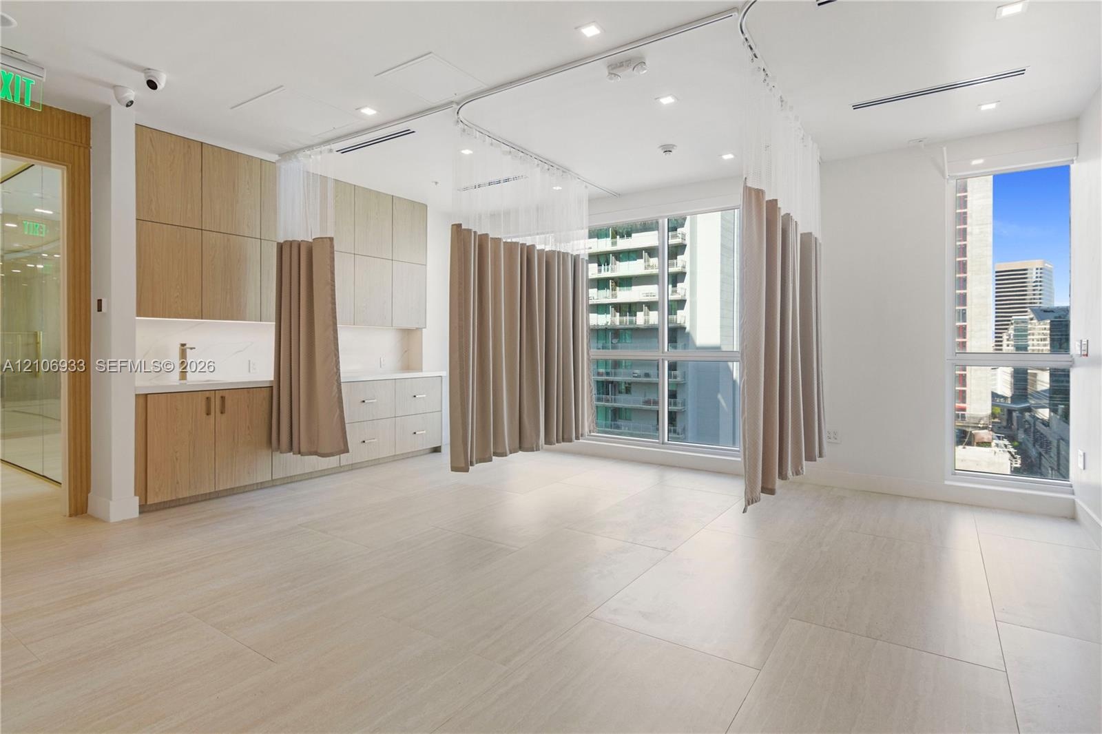 Custom light-finish cabinetry with integrated sink, porcelain tile flooring, ceiling-mounted track systems, recessed lighting, and large windows
