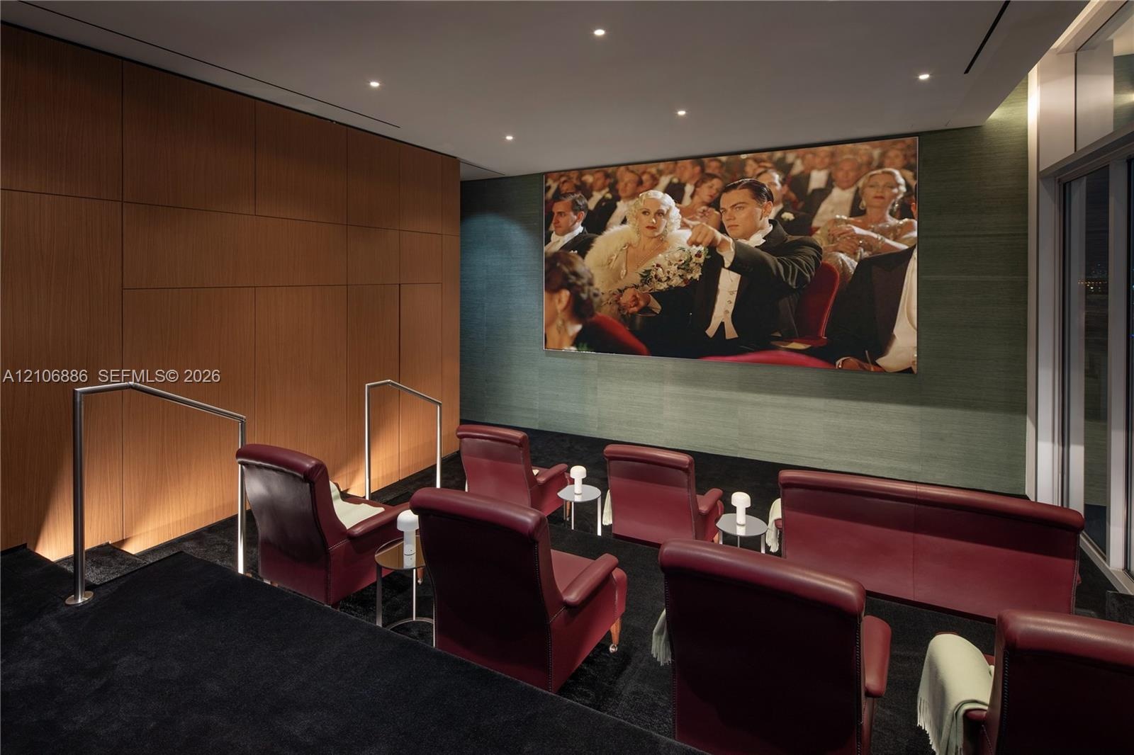 Media room featuring tiered flooring, wood-panel wall accents, recessed ceiling lighting, and integrated wall-mounted projection screen