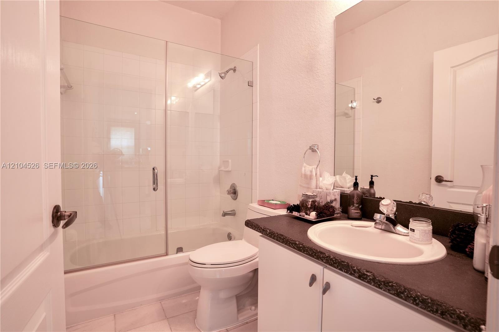 Bathroom featuring a vanity with a dark countertop and integrated sink, a glass-enclosed shower and tub combination, and wall-to-wall mirror
