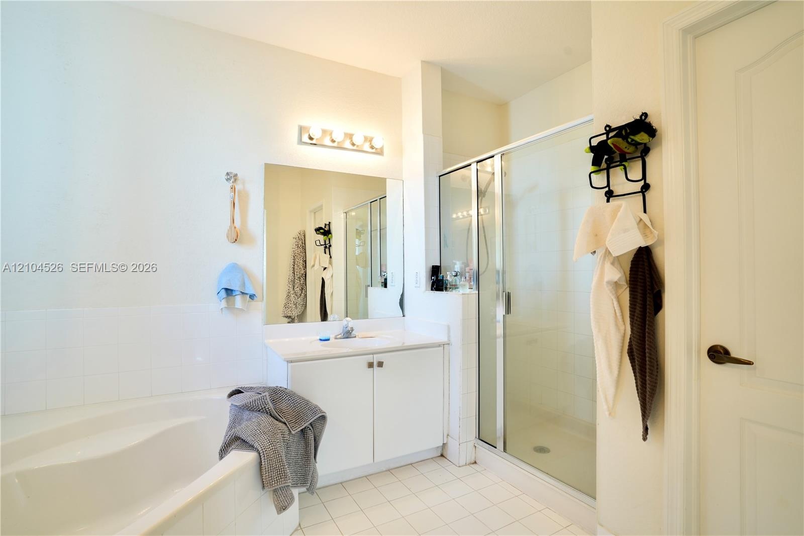 Bathroom featuring a soaking tub, glass-enclosed shower, white vanity cabinet with a solid-surface countertop, and ceramic tile flooring