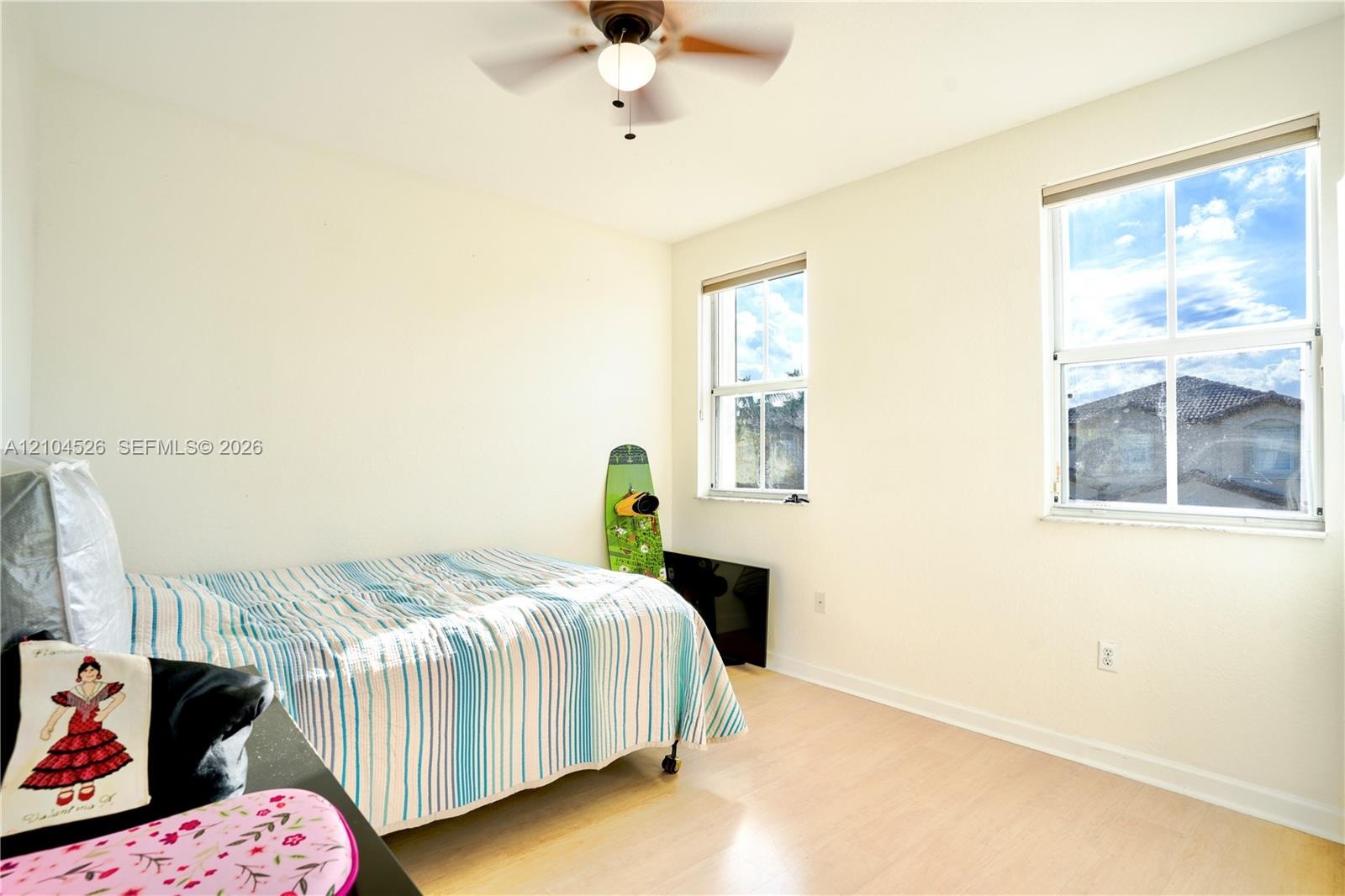 Room featuring light-tone wood-finish flooring, dual windows with blinds, and a ceiling fan with integrated lighting