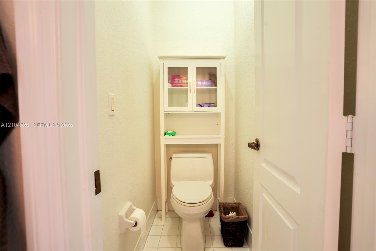 Built-in white storage cabinetry with glass-front upper doors, floor-mounted toilet, and tiled flooring