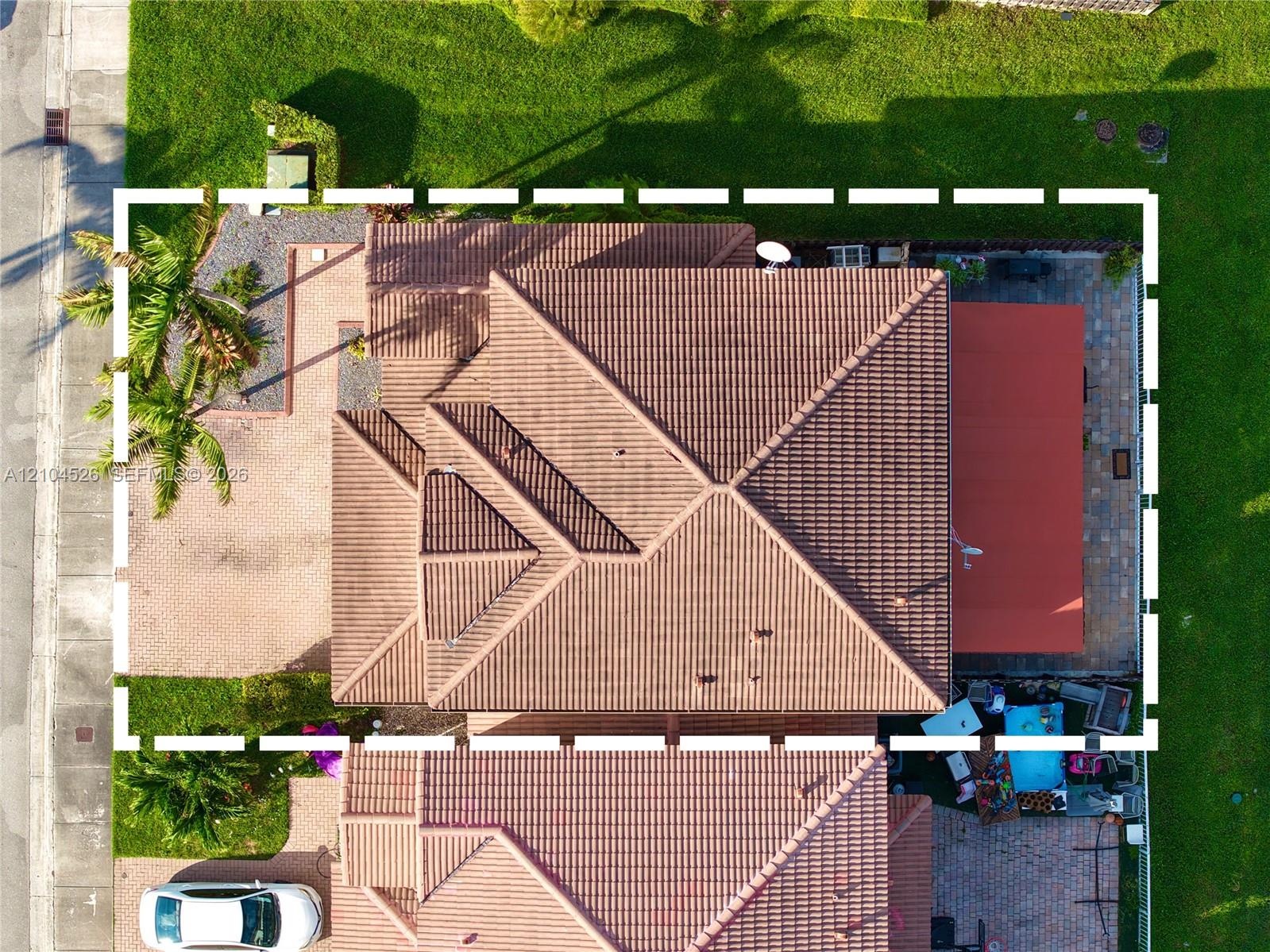 Aerial perspective featuring a multi-hipped tile roof, paved driveway, brick-paver patio, and mature palm landscaping