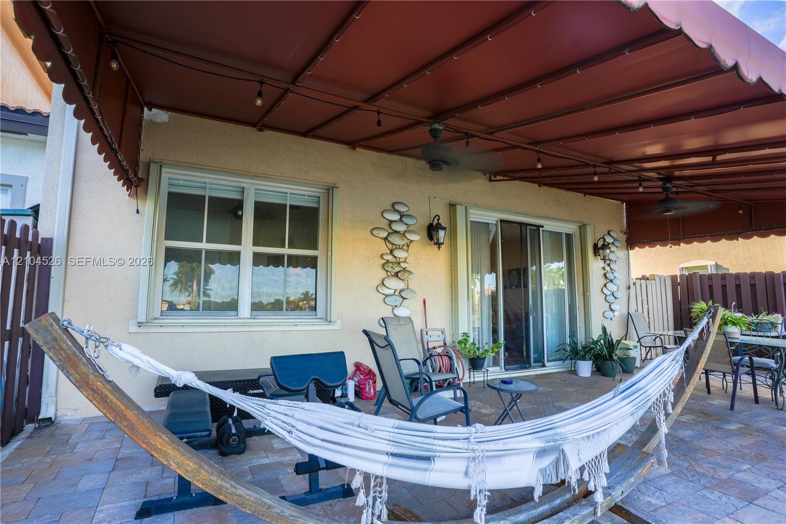 Covered paver patio featuring a retractable awning, dual ceiling fans, wall-mounted light fixtures, and glass sliding doors