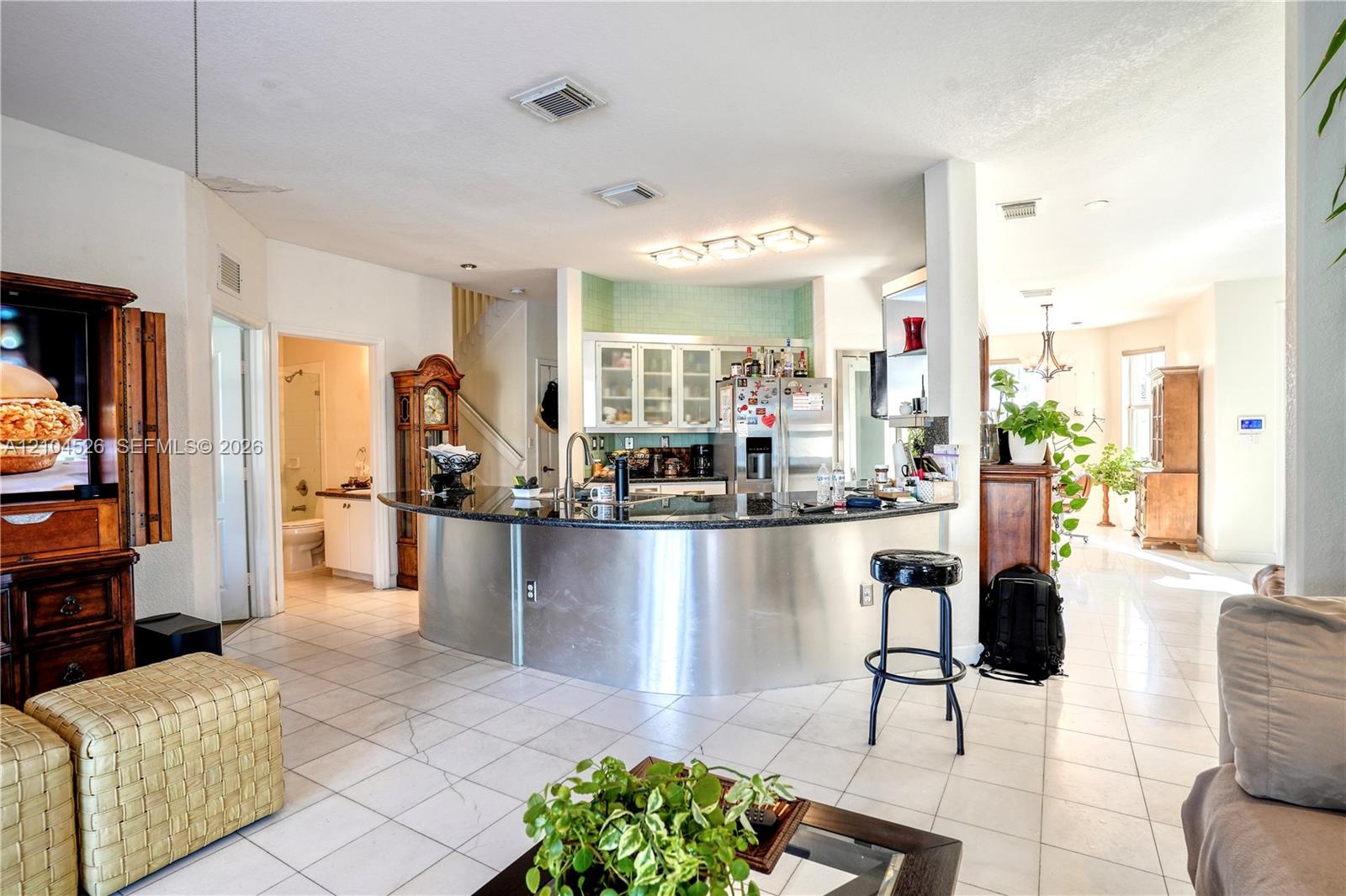 Curved kitchen island featuring a dark stone countertop and stainless steel facade, light-toned tile flooring, recessed ceiling lighting, and white ca