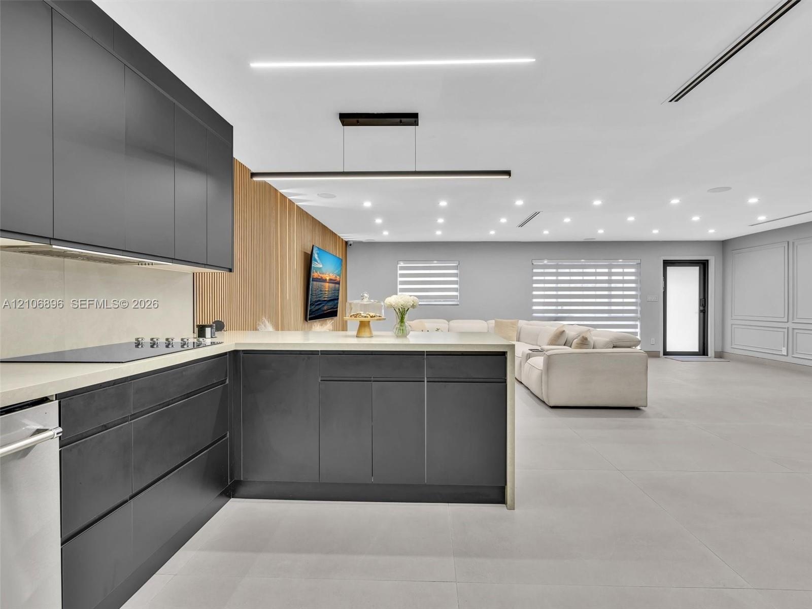 Contemporary kitchen featuring flat-panel charcoal cabinetry, light-toned stone countertops, linear pendant lighting, wood-slat accent wall detailing,