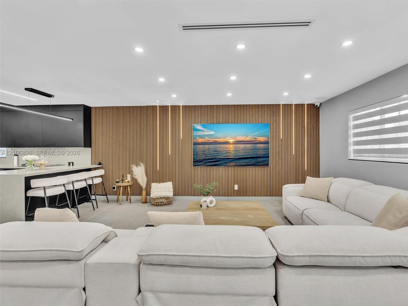 Slatted wood-finish feature wall with integrated vertical lighting, recessed ceiling lighting, linear kitchen island with stone-finish countertop, mat