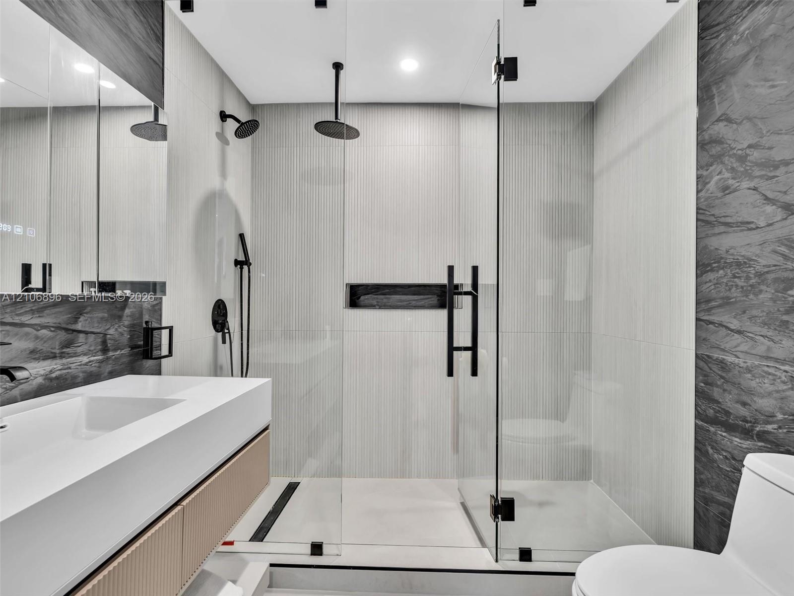 Bathroom featuring a floating vanity with integrated sink, walk-in shower with frameless glass enclosure, dual shower heads including a ceiling-mounte