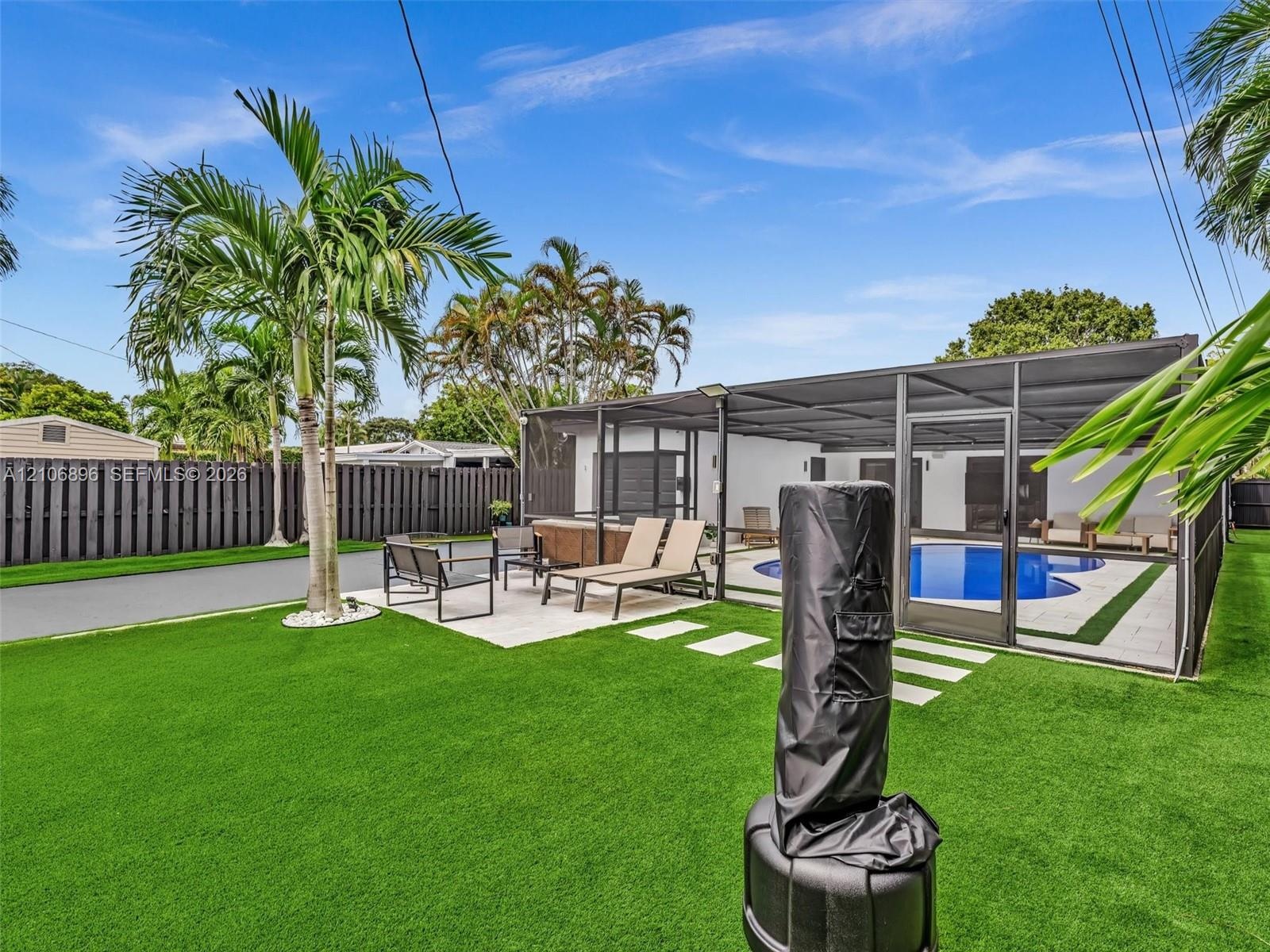 Backyard featuring a synthetic turf lawn, screened-in swimming pool, paved patio area, and perimeter privacy fencing