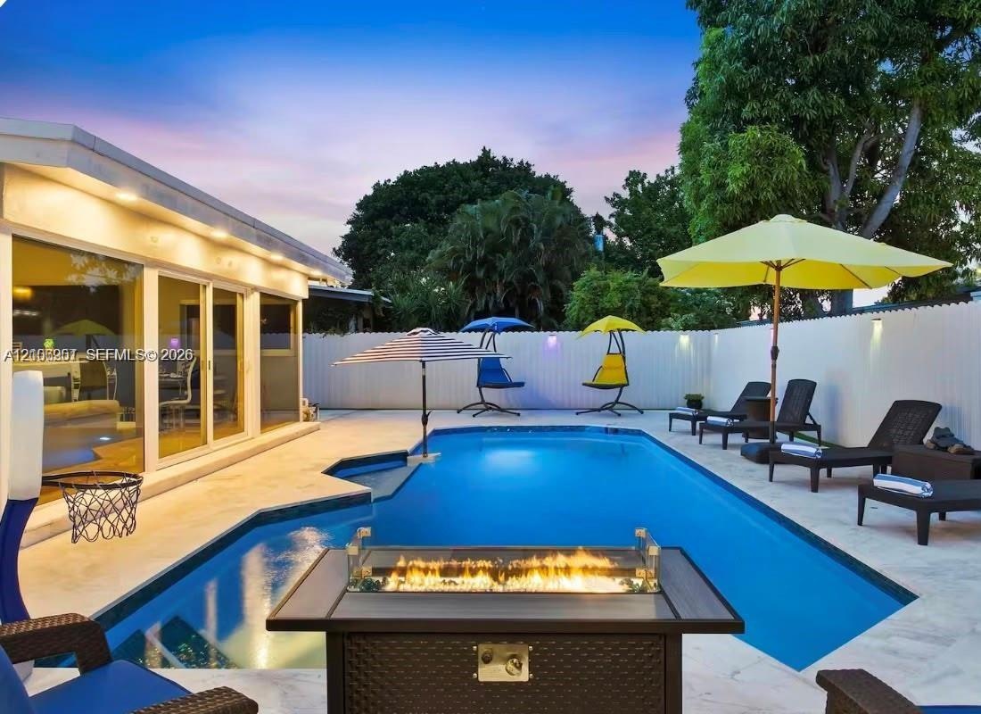 Swimming pool with concrete patio, integrated fire feature, and white perimeter privacy fencing