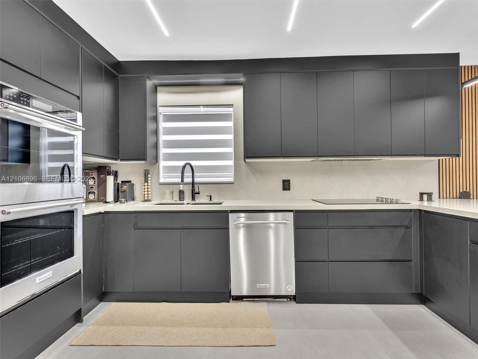 Modern kitchen featuring matte charcoal cabinetry, stainless steel double wall ovens and dishwasher, light-toned solid surface countertops, and linear
