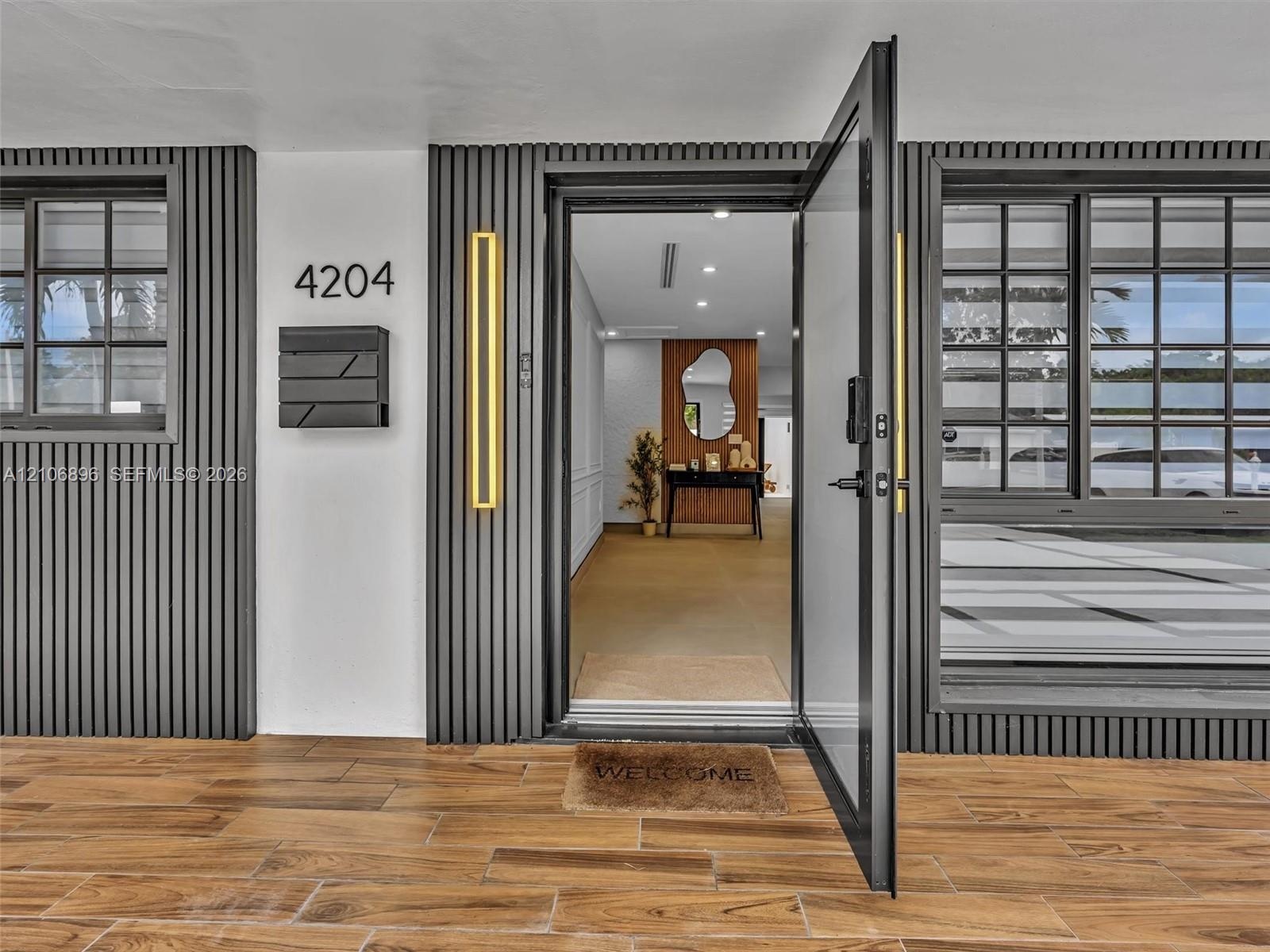 Entryway featuring dark vertical slatted exterior siding, wood-finish tile flooring, matte black grid-pane windows, and dual vertical wall-mounted sco
