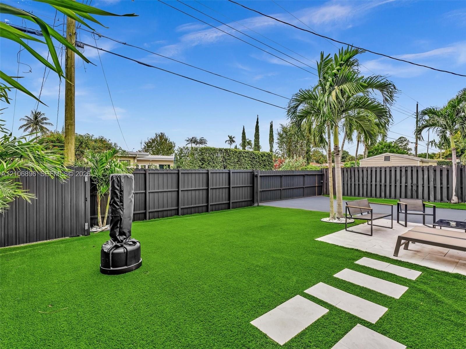 Fenced backyard featuring synthetic turf, paver patio, square concrete stepping stones, and mature palm trees