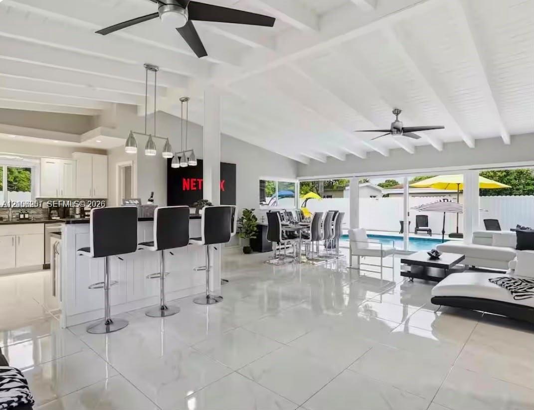Open-concept interior featuring vaulted, beamed ceilings, oversized tile flooring, a kitchen island with stone countertops, and multiple sliding glass