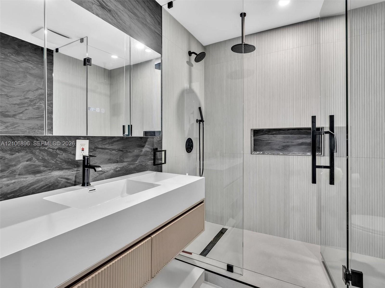 Floating vanity with an integrated sink and textured wood-finish cabinetry, paired with a frameless glass shower enclosure featuring matte black rainf