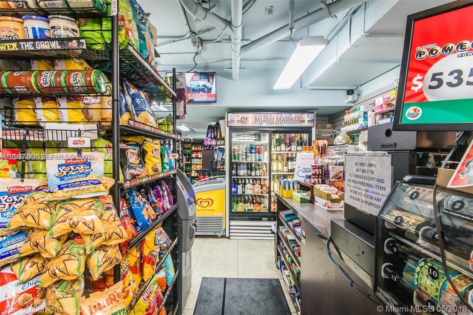 Retail space featuring built-in industrial shelving, commercial glass-front refrigeration units, a stone-surfaced transaction counter, and overhead fl