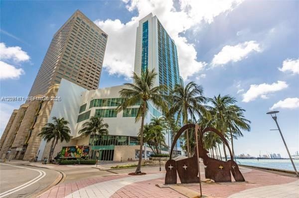 High-rise building with glass facade, paved pedestrian plaza, native palm trees, and waterfront hardscaping
