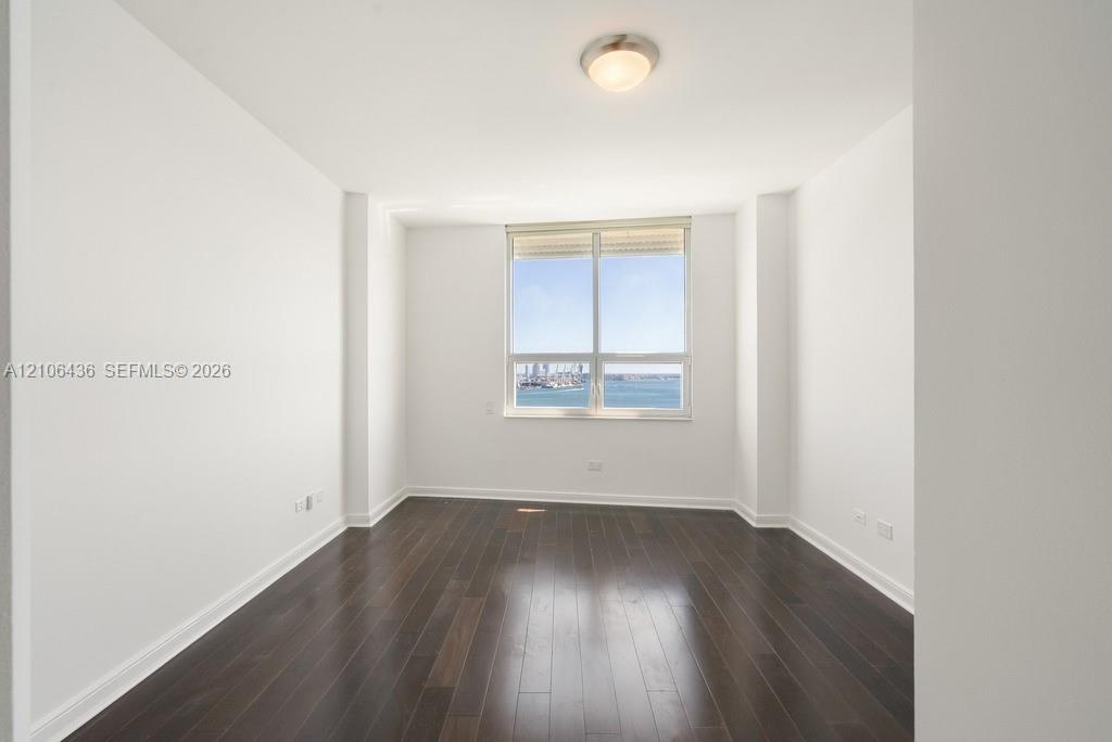 Room featuring wood-finish flooring, white walls, and a large window showcasing water and harbor scenery, complemented by a flush-mount ceiling light 