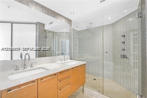 Dual-sink vanity with light-tone cabinetry and stone countertop, complemented by a walk-in glass-enclosed shower featuring multi-head wall-mounted fix
