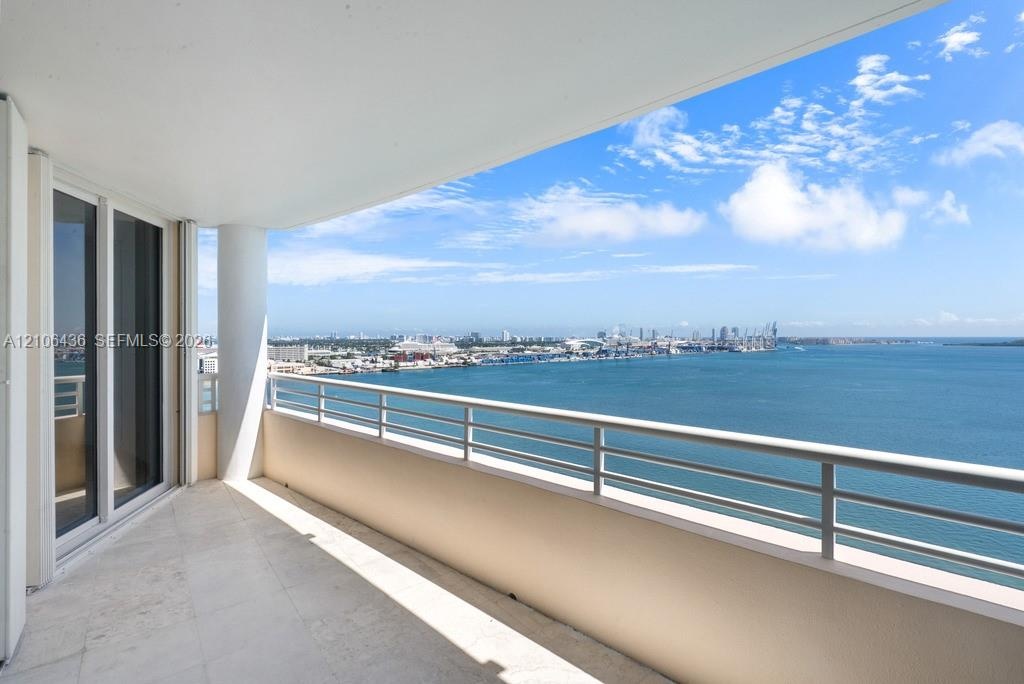 Covered balcony featuring stone-finish flooring, a sleek metal railing, a structural support column, and floor-to-ceiling glass sliding doors