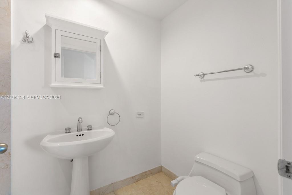 Pedestal sink with polished chrome fixtures, wall-mounted medicine cabinet with crown molding, and stone-finish flooring