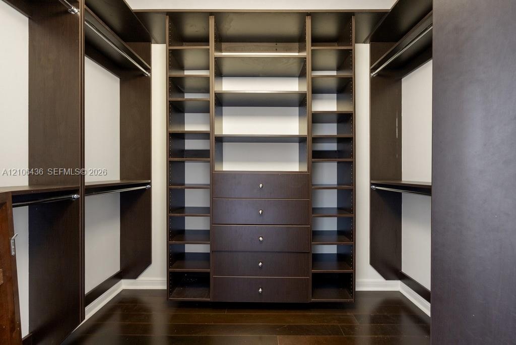 Custom walk-in closet featuring dark wood-finish cabinetry, integrated open shelving, a center bank of five soft-close drawers with metallic pulls, an