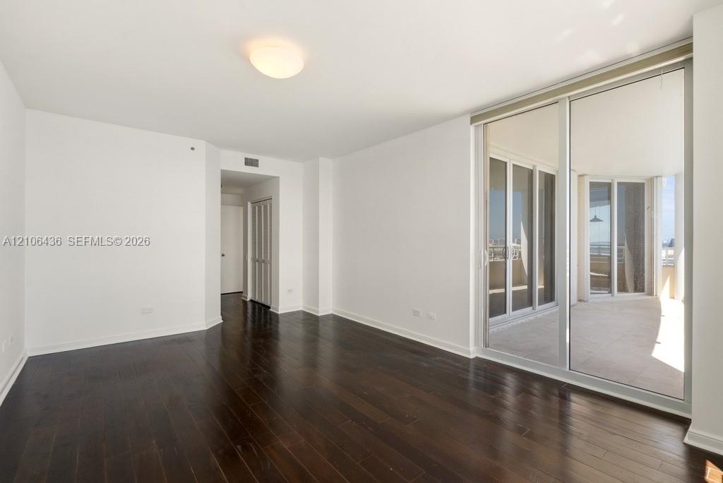 Interior space featuring dark wood-finish flooring, floor-to-ceiling glass sliding doors, and a private balcony with exterior railings