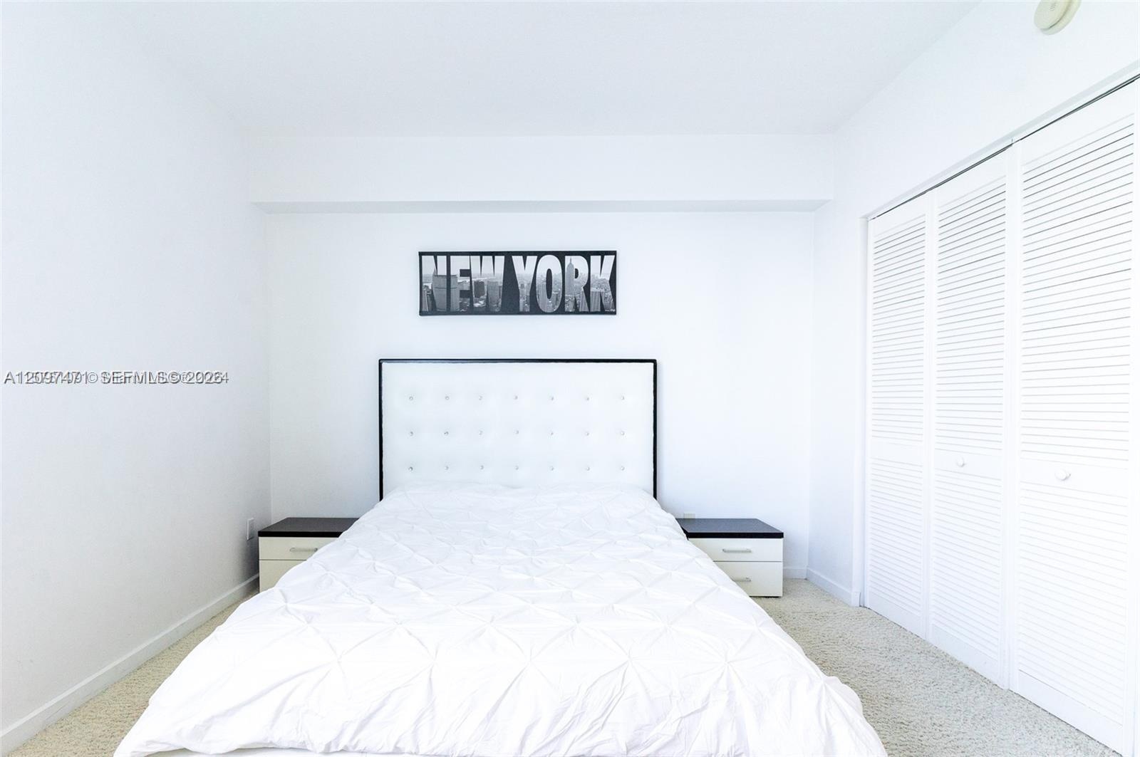Neutral-toned carpeting, white walls, and a built-in closet with white louvered doors