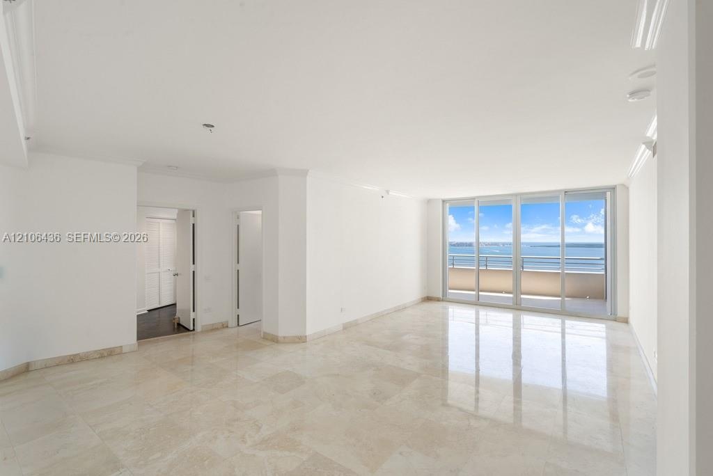 Open-concept interior featuring light-toned stone tile flooring, crown molding, and floor-to-ceiling glass sliding doors providing water scenery and a