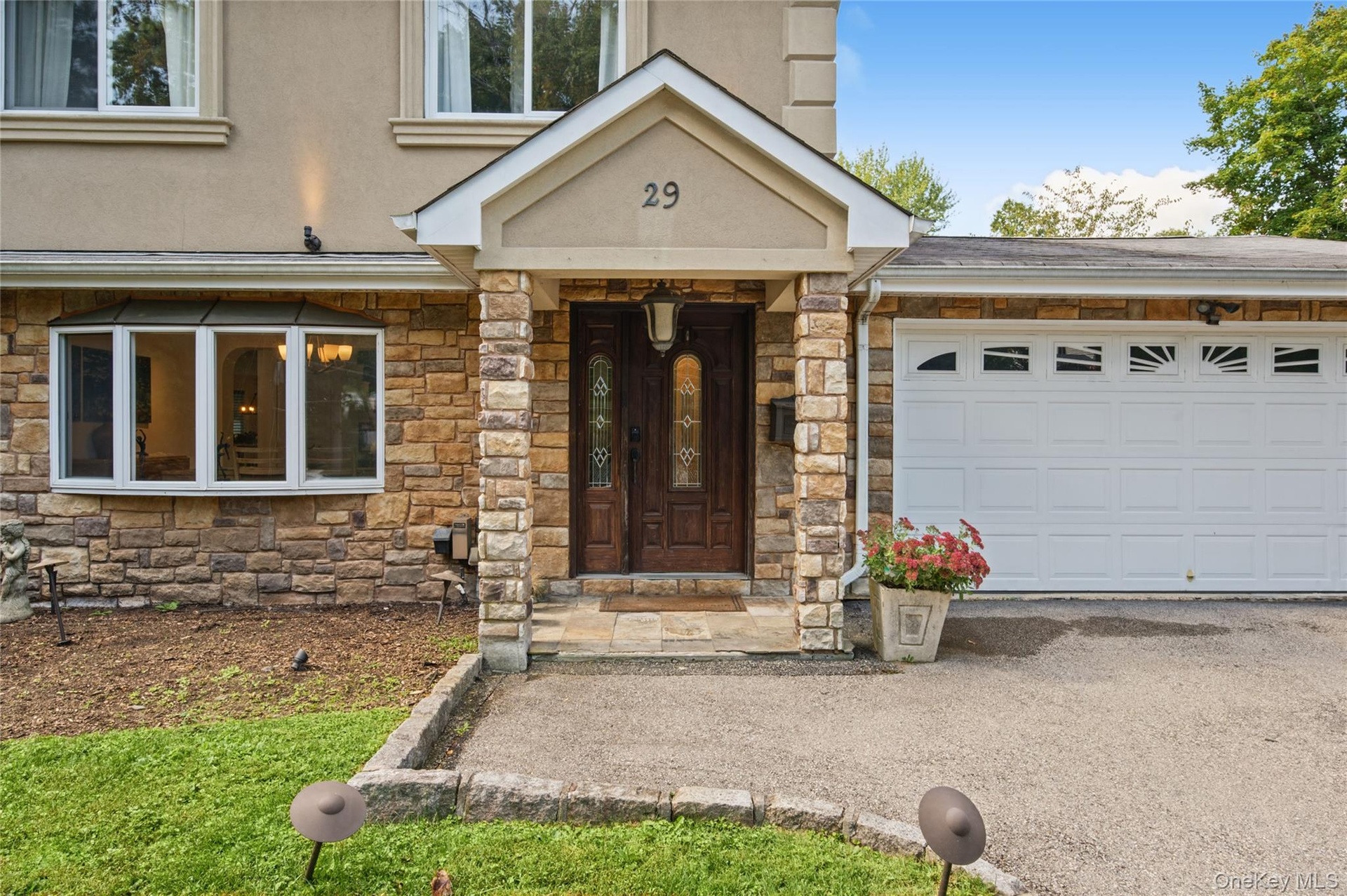 Exterior facade featuring stacked stone masonry, a covered entryway with structural stone pillars, a double-door entry with leaded glass accents, a mu