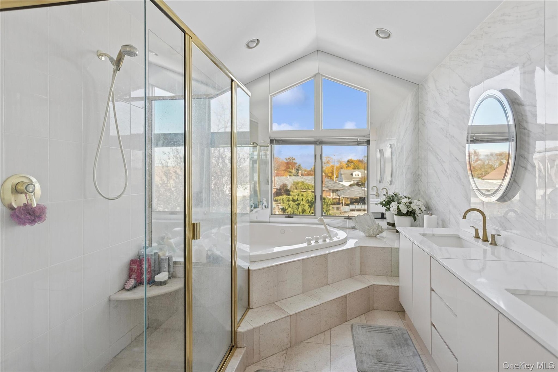 Full bath with double vanity, lofted ceiling, a garden tub, a shower stall, and plenty of natural light