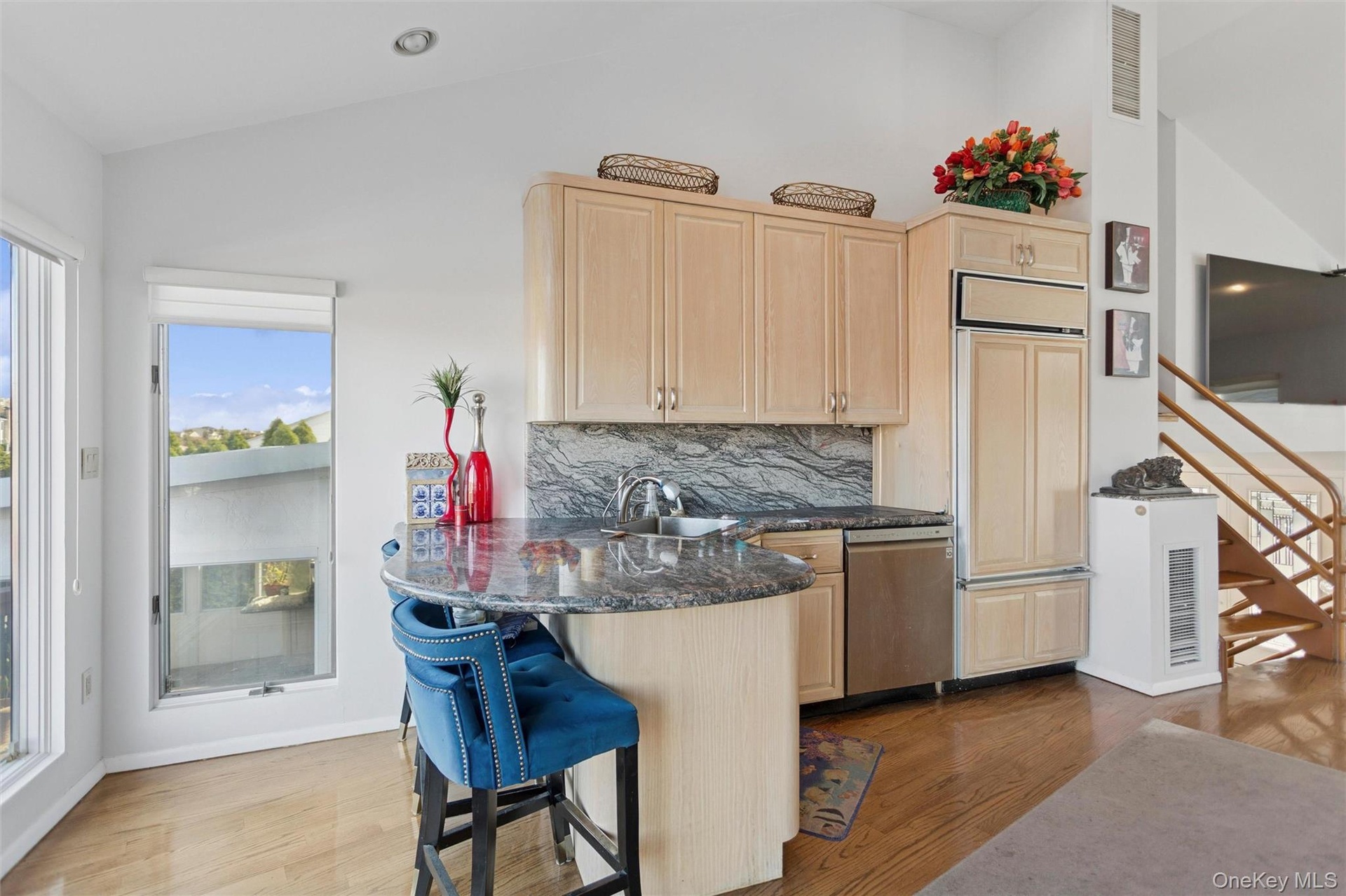 Kitchen with light brown cabinetry, dark wood-type flooring, a breakfast bar area, backsplash, and paneled fridge