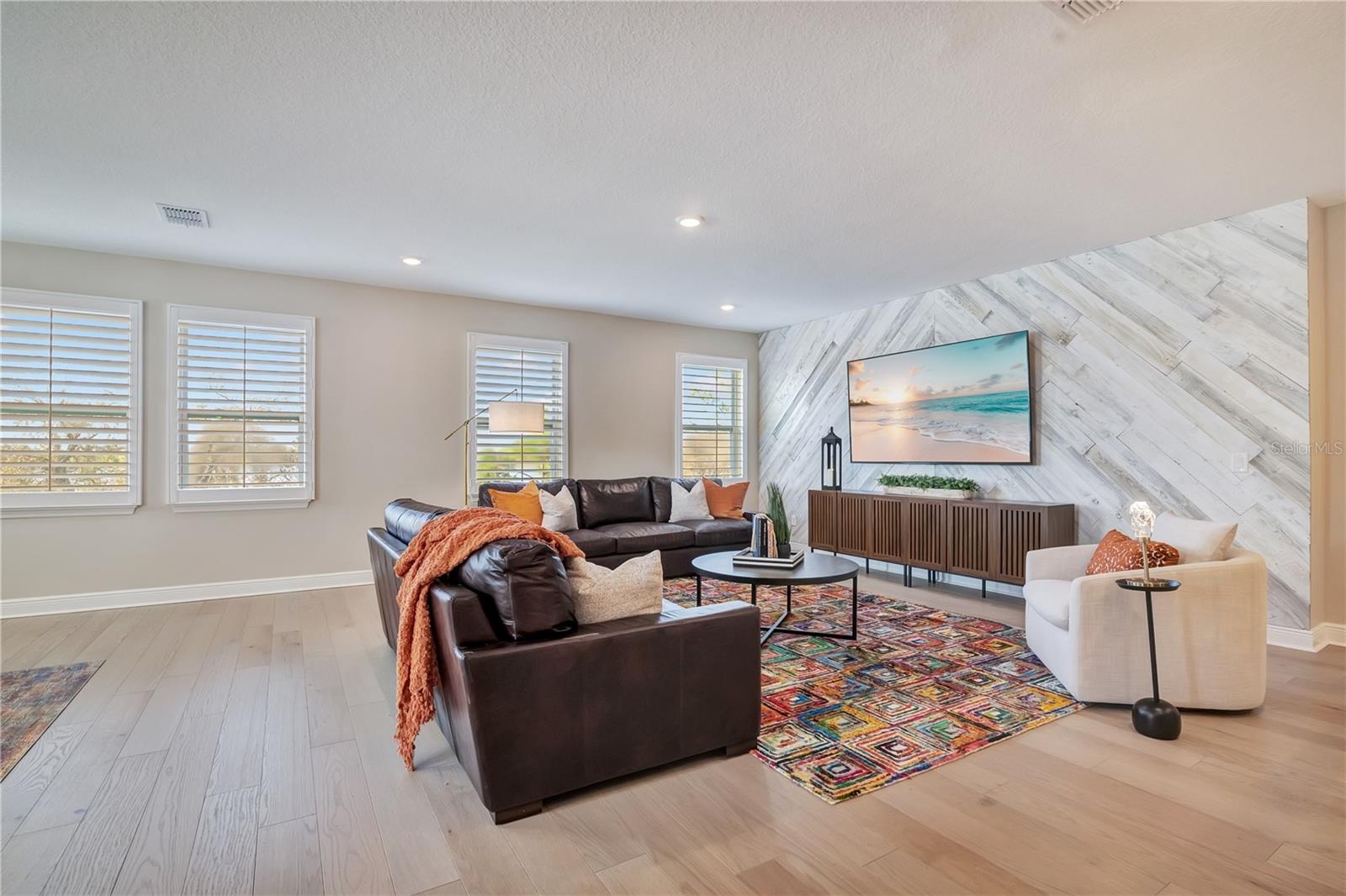 Spacious loft featuring a statement accent wall, recessed lighting and plantation shutters.