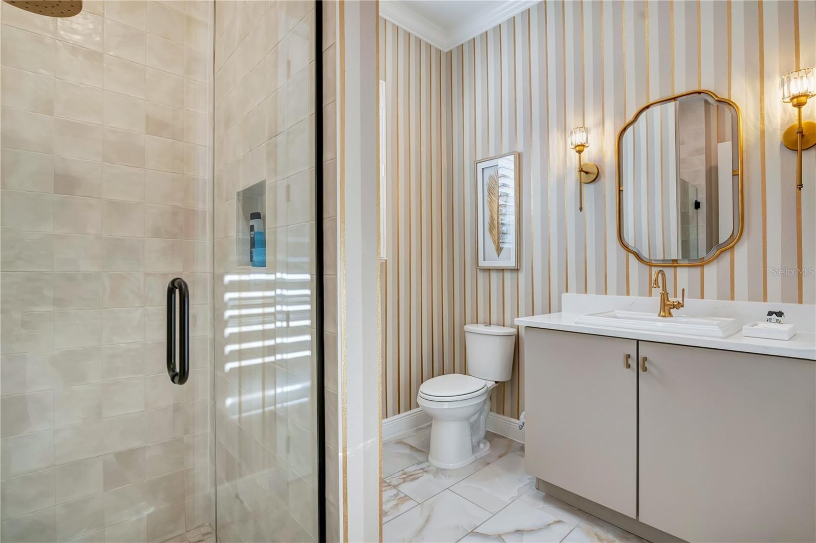 Designer bathroom with a glass-enclosed shower, striped accent wall and gold-tone fixtures.