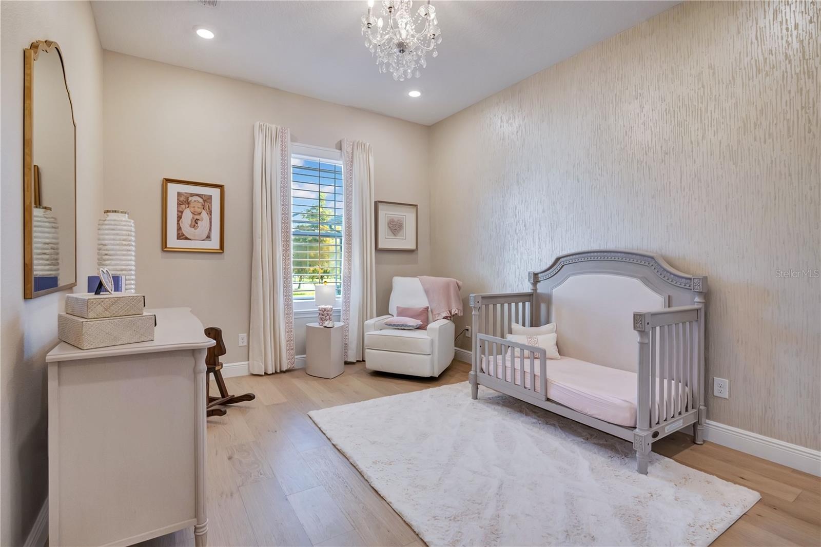 Charming bedroom featuring hardwood flooring, a decorative accent wall and chandelier lighting.