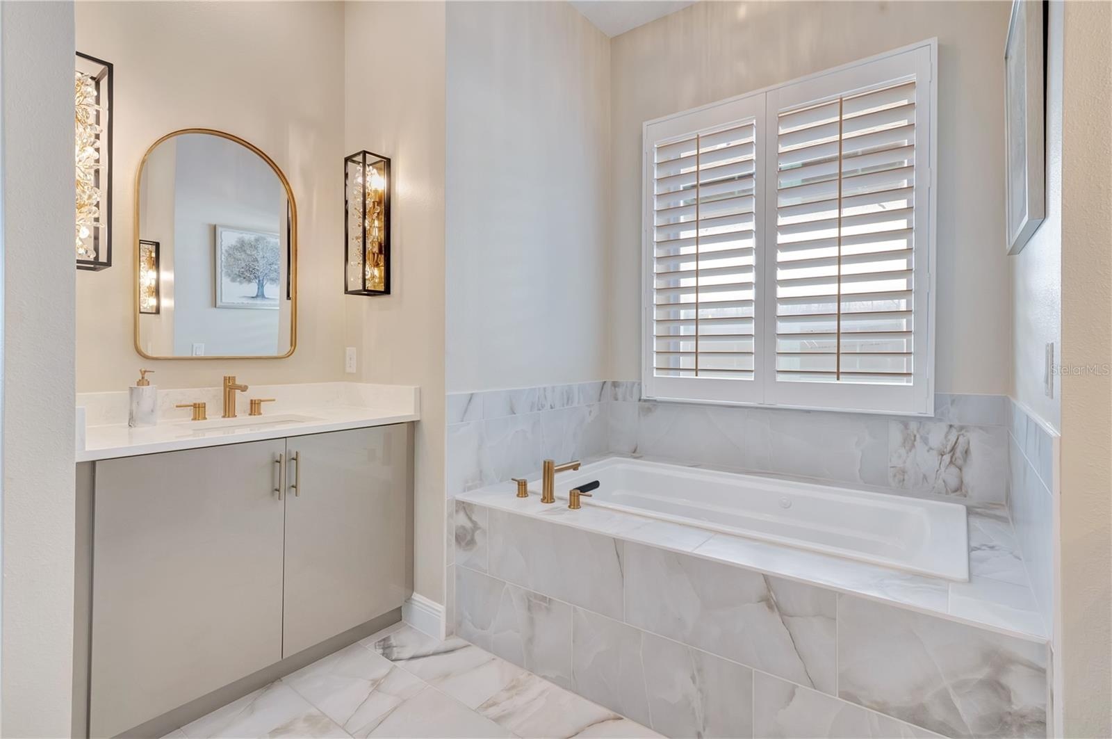 Elegant bathroom featuring a soaking tub, upgraded tile surrounds and a vanity accented by designer sconces.