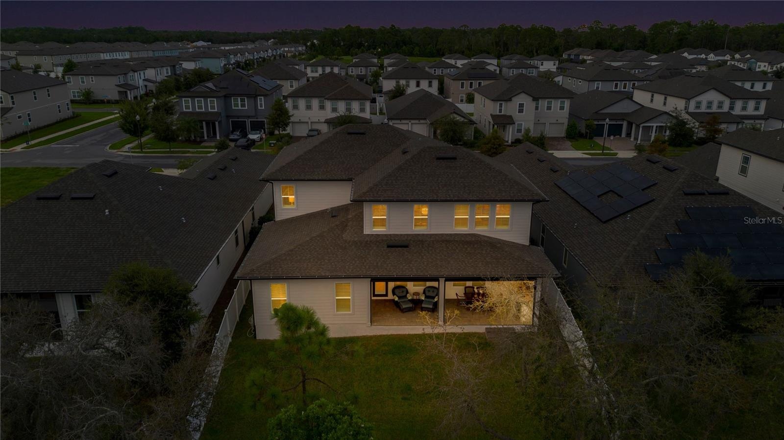 Rear aerial at twilight captures the backyard and warmly illuminated covered lanai.