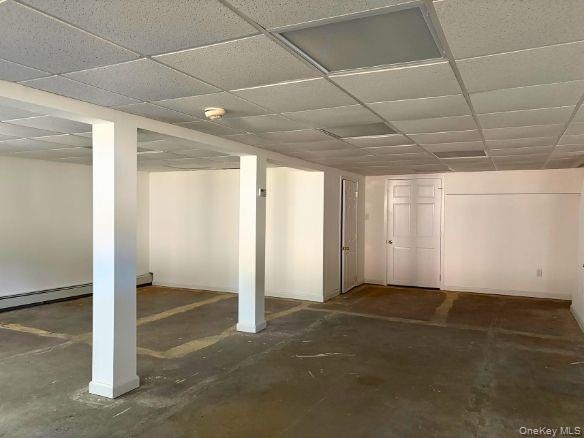 Open-concept partially finished basement space featuring white walls, drop ceiling panels, structural support columns, recessed windows, and closed of