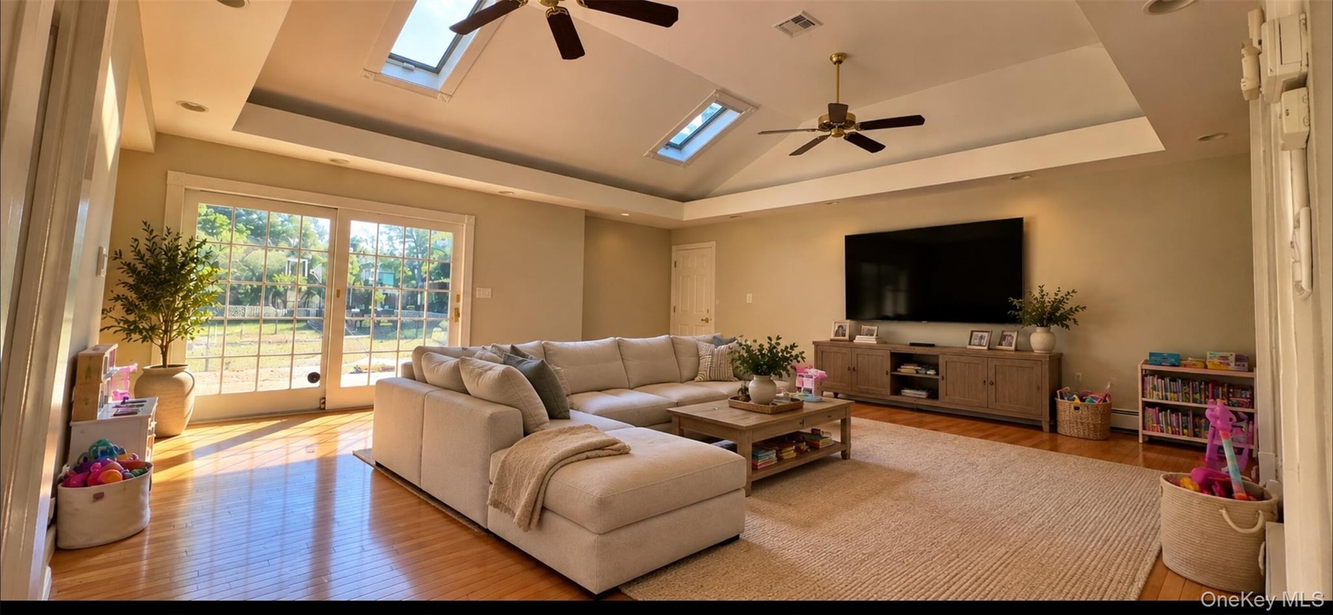AI Enhanced Photo: Virtually stagedLiving area featuring a tray ceiling with dual skylights, wood-finish flooring, two ceiling fans, and sliding glass