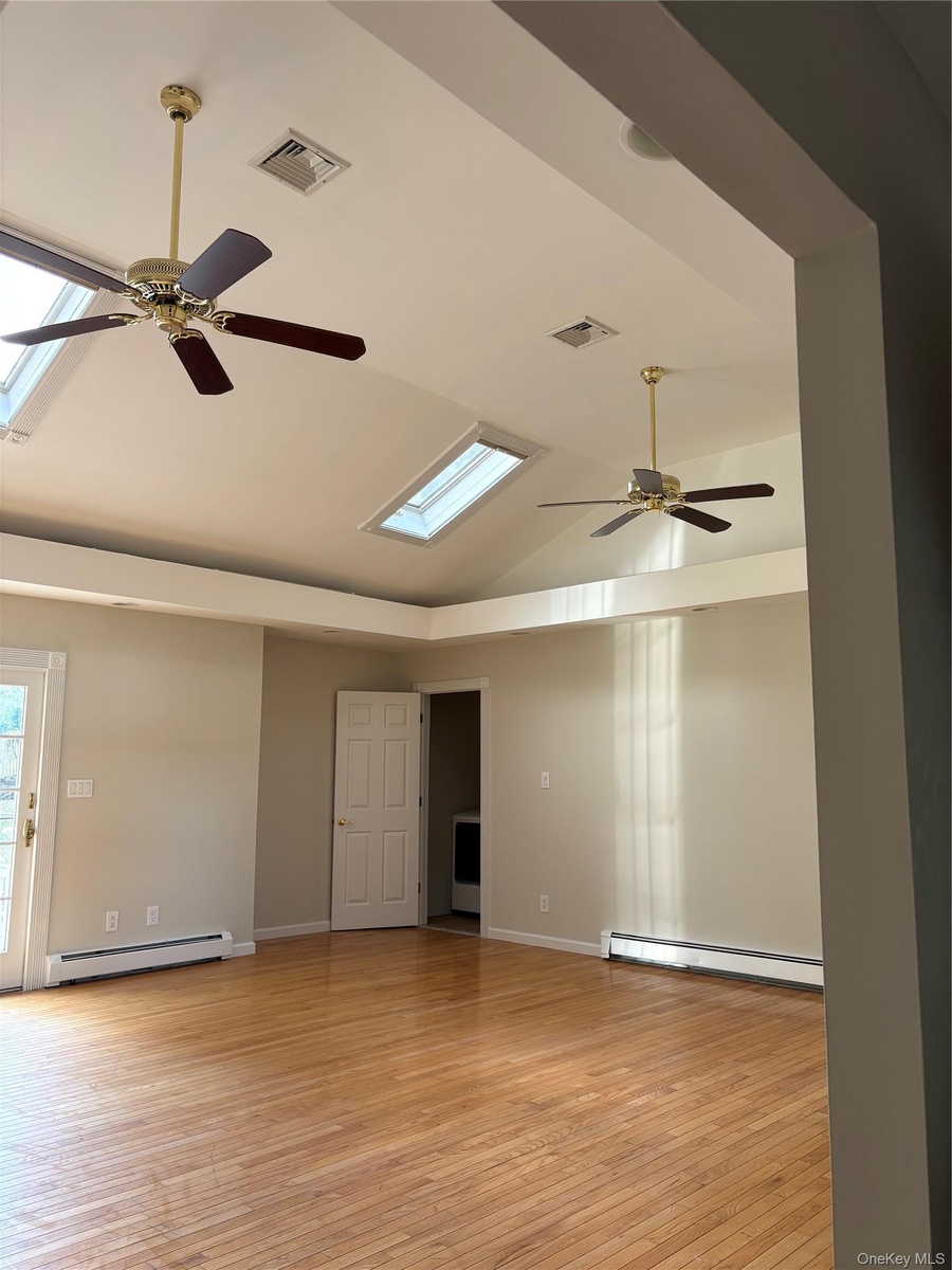 Vaulted ceilings featuring dual skylights, wood-finish flooring, and matching multi-blade ceiling fans. Slicing glass doors to the patio and laundry r