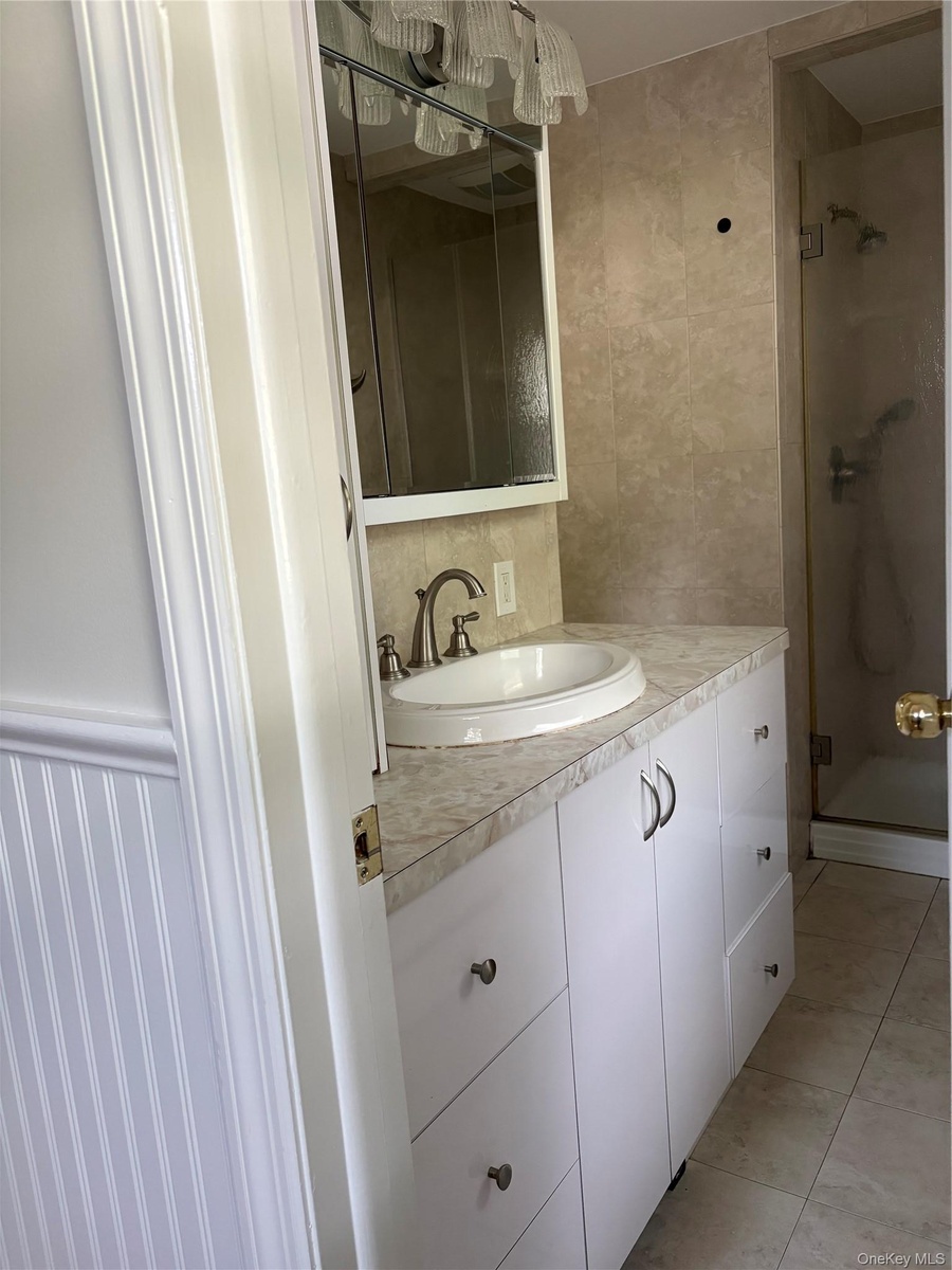 Bathroom featuring white cabinetry, stone-finish countertop, integrated sink, mirrored medicine cabinet, and tiled shower enclosure