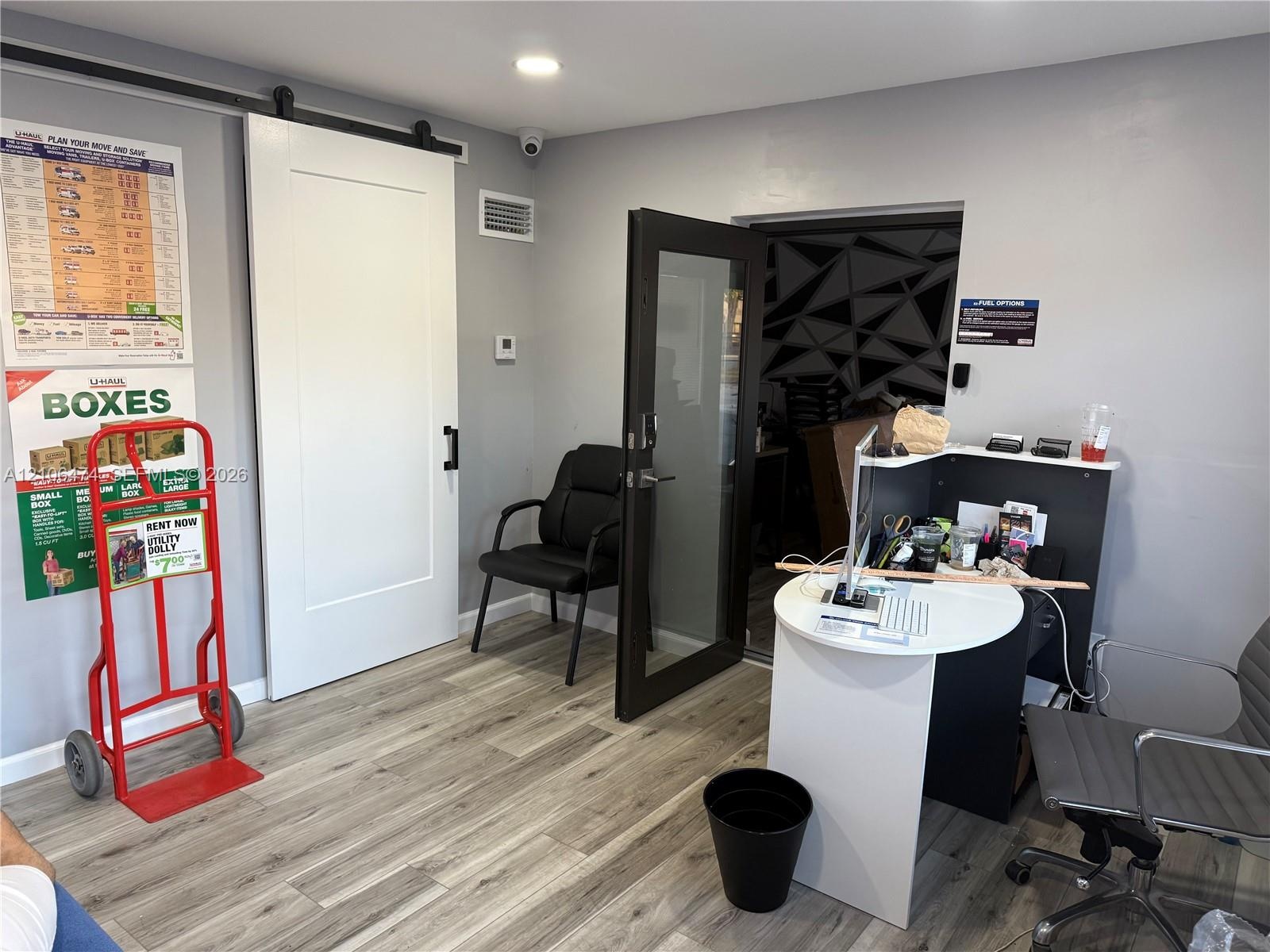 Interior space featuring wood-finish flooring, white shaker-style sliding barn door with black hardware, and a dark-framed glass panel door with integ